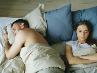 Tense couple lying apart in bed, reflecting relationship strain